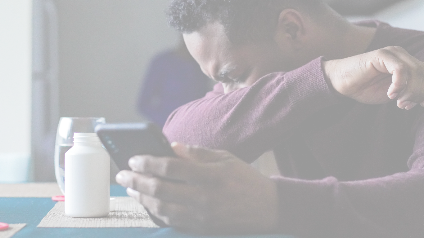 A man sitting down has a cell phone in his left hand and uses his right elbow to cover his mouth while sneezing, alluding to the important tips regarding indoor air quality that are being shared from Dr Comfort Cooling and Plumbing